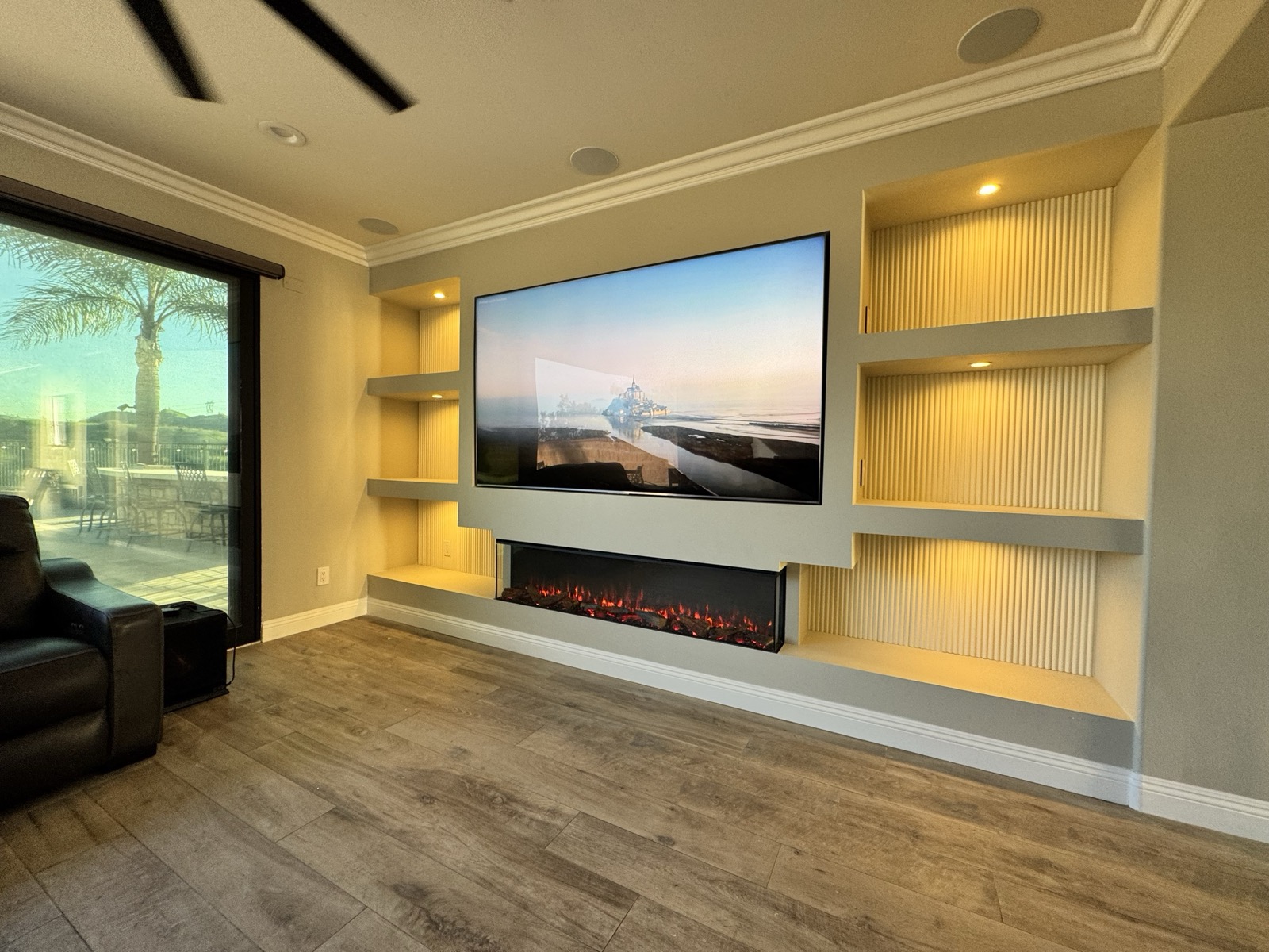 Fluted oak media wall with lit niches and a linear fireplace, seen from the side